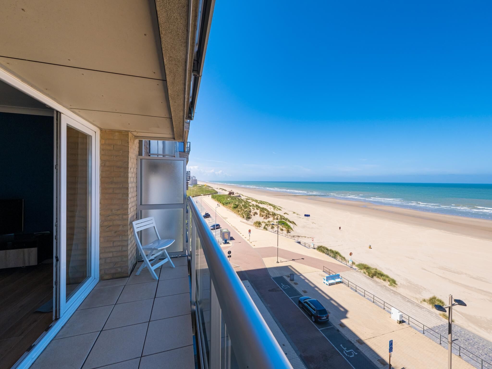 A balcony with a view of a beach and a parking area.