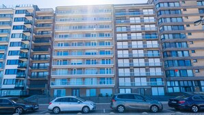 Un immeuble résidentiel à plusieurs étages, doté de balcons, un espace de stationnement avec des voitures et un ciel dégagé.