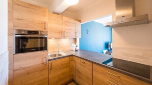 Une cuisine moderne avec des armoires en bois, un four encastré, une hotte en acier inoxydable et un mur d’accent bleu.