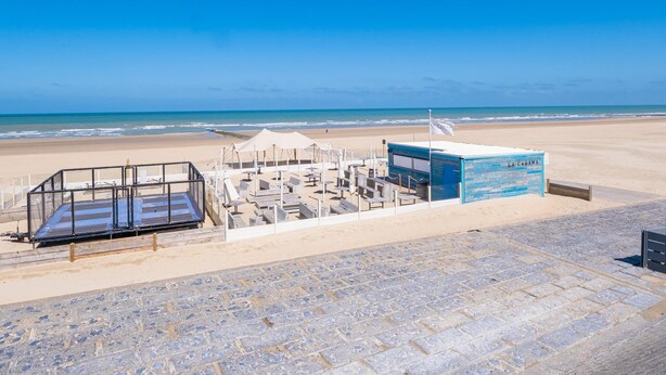 Une zone aménagée au bord de la plage, comprenant un poste de surveillance pour les sauveteurs, un espace de repos couvert et une promenade dallée.