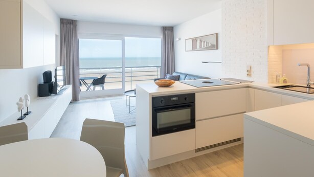 A modern kitchen with a built-in oven, a dining area with a table and chairs, and a view of the beach through large windows. - Studio on the 4th floor with sea view (Middelkerke)