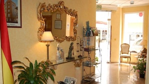 A reception area with a mirror, a lamp, a statue, a plant, and a magazine rack. - Hotel Albohera Playa by Belvilla Resorts-suite (San Javier)