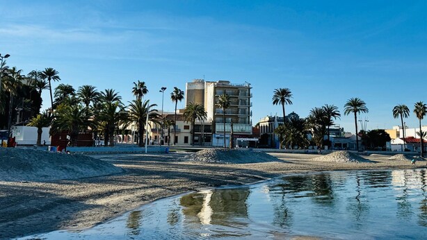 A beach with palm trees, a building with multiple floors, and a clear sky. - Hotel Albohera Playa by Belvilla Resorts-suite (San Javier)