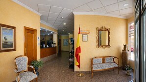 A lobby with a reception desk, a flag, a sofa, a chair, and a mirror on the wall. - Hotel Albohera Playa by Belvilla Resorts-suite (San Javier)