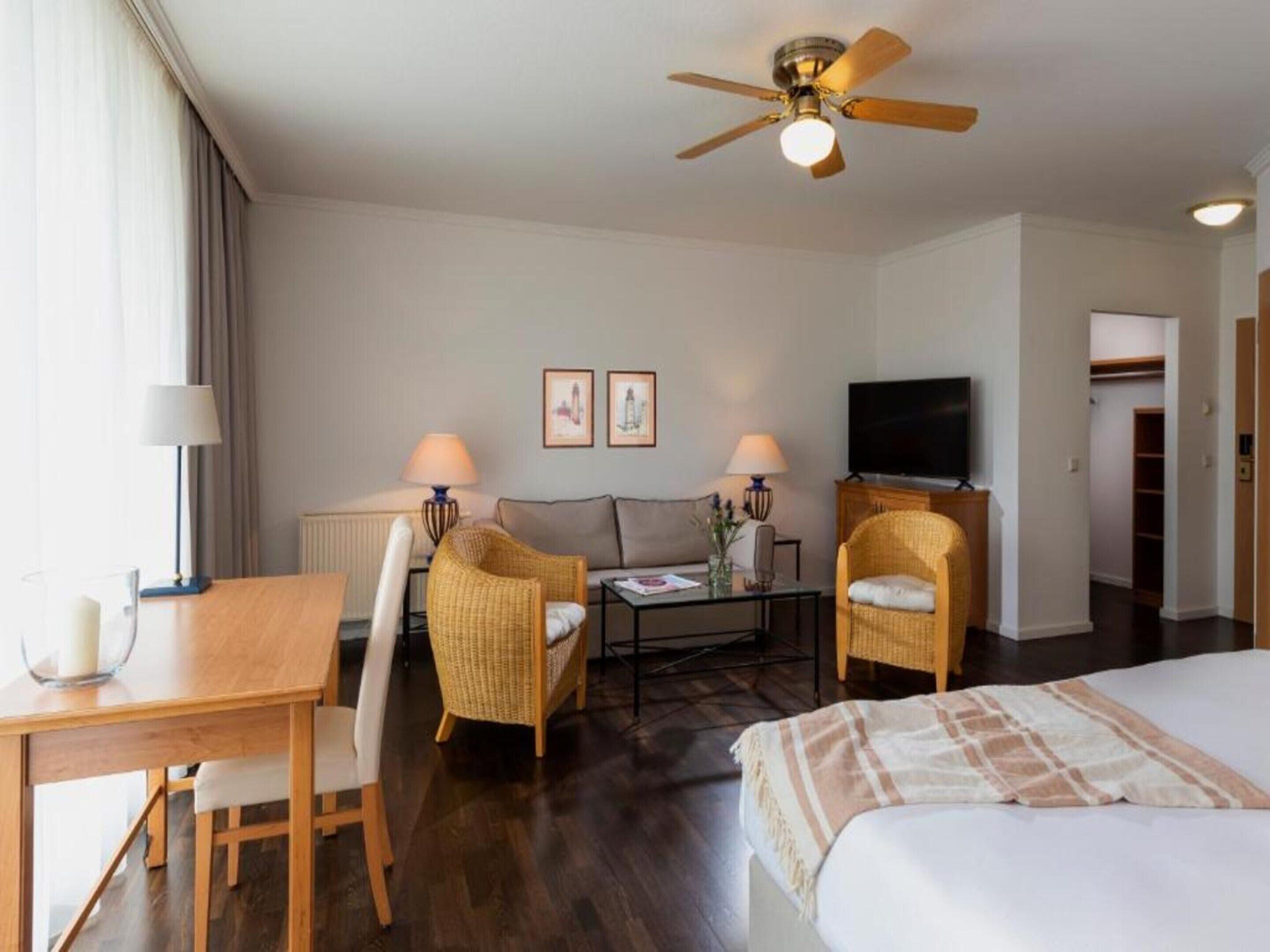 Habitación de hotel con cama, escritorio, dos sillas, televisión y ventilador de techo.