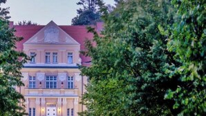 A large, stately building with a symmetrical facade, a central entrance, and a well-maintained garden with a paved pathway leading to the entrance. - Sunday Resort Rugen Suites (Sagard)