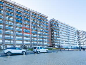 A modern high-rise building with multiple balconies, a paved ground floor, and parked cars. - Beautiful apartment on the 4th floor with garage (Middelkerke)