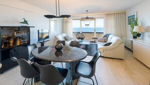 A modern living room with a dining area, a sofa set, a TV, and a view of the sea. - Beautiful apartment on the 4th floor with garage (Middelkerke)
