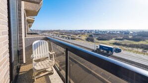 A balcony with two Adirondack chairs, a view of a highway, and a distant town. - Beautiful apartment on the 4th floor with garage (Middelkerke)