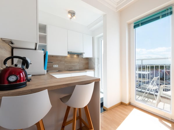 A modern kitchen with a red kettle, white chairs, and a large window with a view of parked cars.