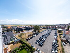 A parking lot with rows of cars, surrounded by buildings and greenery.