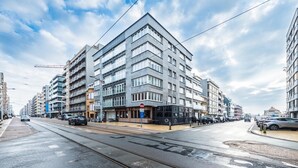 Een moderne straat in de stad met meerlaagsgebouwen, een tramlijn en geparkeerde auto's.