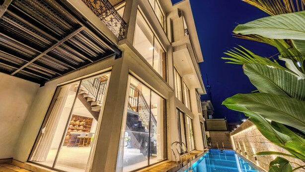 A modern building with a swimming pool, large windows, and a staircase leading to the upper floors. - ELIVAAS Valley View 5BHK Villa With Pool (Mapusa)