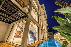 A modern building with a swimming pool, large windows, and a staircase leading to the upper floors. - ELIVAAS Valley View 5BHK Villa With Pool (Mapusa)