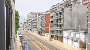 A multi-story residential building with balconies, a tram line, and parked cars. - Retro studio with sleeping area (Middelkerke)