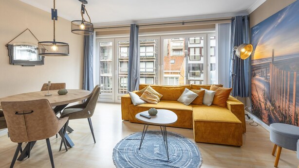 A modern living room with a sofa, dining table, chairs, and a large window with curtains. - Retro studio with sleeping area (Middelkerke)