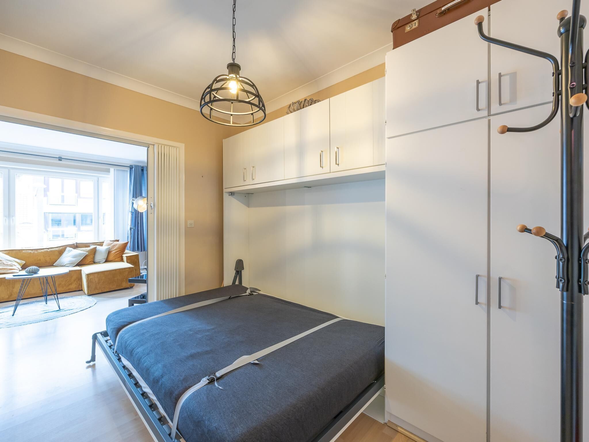 A modern bedroom with a bed, wardrobe, and a view of the outside.