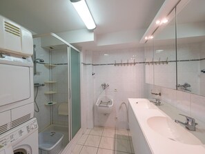 Um banheiro moderno com máquina de lavar, chuveiro, vaso sanitário e uma pia grande.