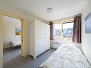 Quarto com cama, guarda-roupa, radiador, janela com cortinas e um quadro na parede.