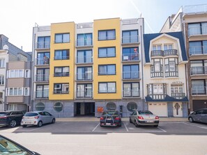 Um edifício residencial com vários andares, varandas, uma garagem e diversos carros estacionados.