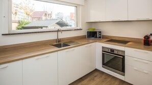 A modern kitchen with white cabinets, a stainless steel sink, a microwave, and an oven. - Luxury holiday home by the sea (Middelkerke)