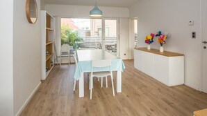A bright kitchen with a wooden floor, white cabinets, a dining table with chairs, a blue pendant light, and a vase with flowers on a counter. - Luxury holiday home by the sea (Middelkerke)