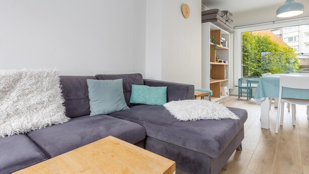 A modern living room with a grey sofa, a wooden coffee table, and a view of a dining area with a table and chairs. - Luxury holiday home by the sea (Middelkerke)