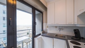 Une cuisine moderne avec des armoires blanches, une cuisinière intégrée et une vue sur la plage grâce à une grande fenêtre.
