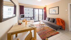 Un salon moderne avec un canapé, un téléviseur, une table à manger et un tapis coloré.