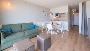 Een modern appartement met een groene bank, een witte eettafel en een kitchenette.