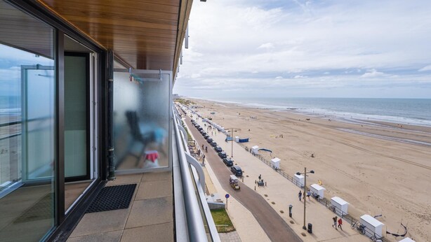 Een balkon met uitzicht op een strand, een parkeerplaats en een heldere lucht.