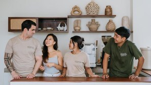 Un grupo de personas de pie junto a una barra en una habitación con estanterías que muestran cerámica y una máquina de café.