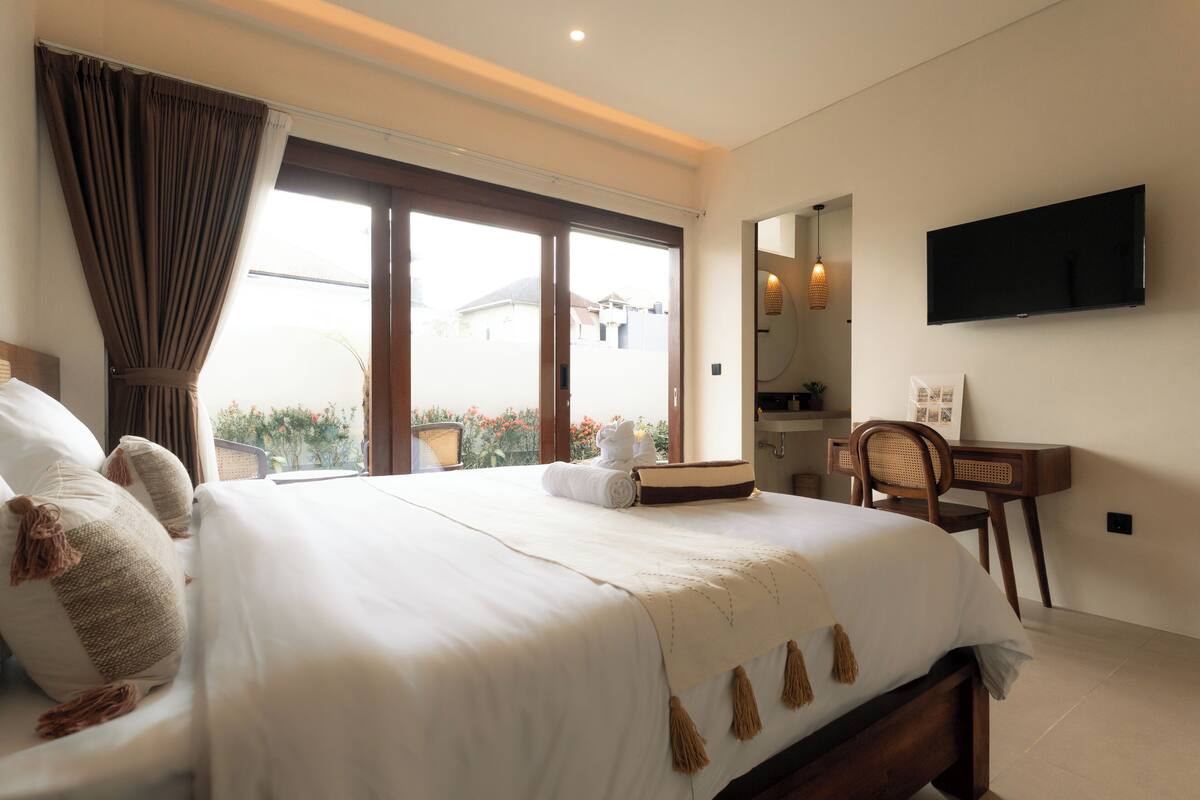 A hotel room with a large bed, a desk, a TV, and a view of the outside.