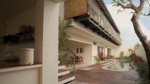 Una casa moderna con terraza de madera, piscina y una escalera que lleva a un balcón.