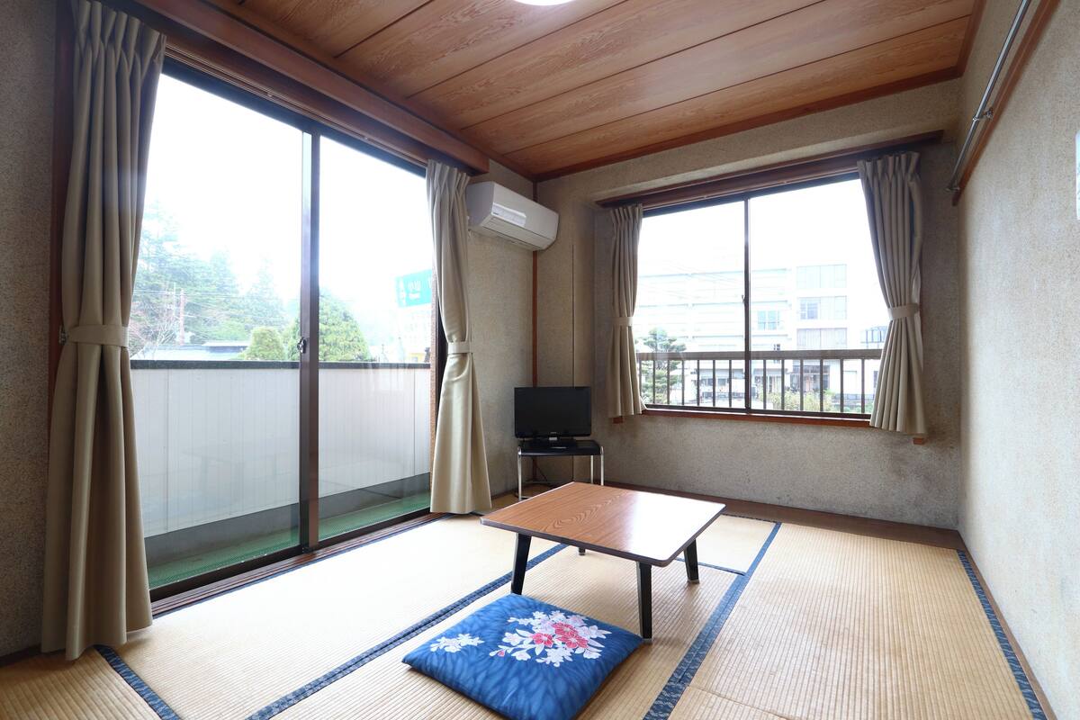 A room with tatami flooring, a low table, a cushion, and a television.