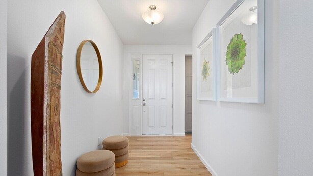 A hallway with a wooden floor, a white door, and a wall-mounted mirror. - Marbella Lane - 7BR Home w Mountain Ocean Views (Waianae)