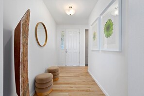 Un pasillo con suelo de madera, una puerta blanca y un espejo fijado a la pared.