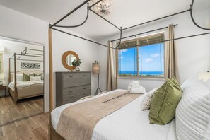 A bedroom with a four-poster bed, a dresser, a mirror, and a view of the sea. - Marbella Lane - 7BR Home w Mountain Ocean Views (Waianae)