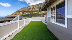 A residential property with a small artificial lawn, white exterior walls, and a view of a mountainous landscape. - Marbella Lane - 7BR Home w Mountain Ocean Views (Waianae)
