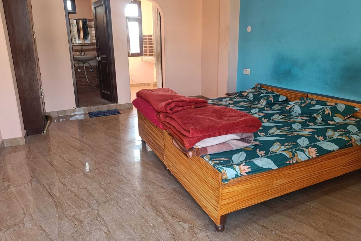 A room with a wooden bed, a red blanket, a floral bedspread, and a tiled floor.