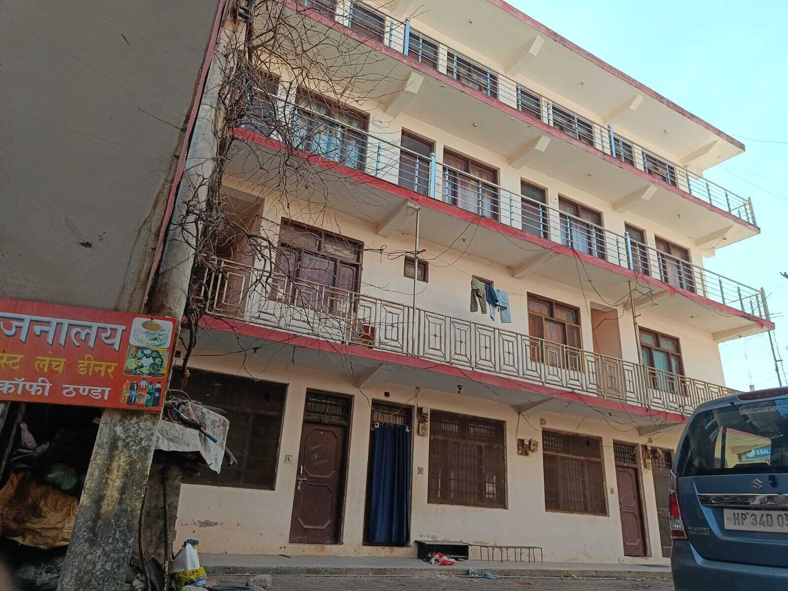 Un edificio de varios pisos con balcones, un cartel y un automóvil estacionado.