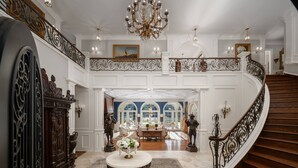 Ein prächtiger Eingangsbereich mit Treppe, aufwendiger Geländer, einem Chandelier und einem Essbereich mit Aussicht.