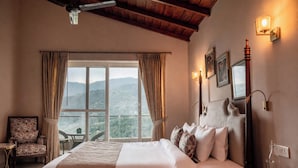 A hotel room with a large bed, a chair, a table, and a view of the mountains. - amã Stays & Trails Aryananda Villas, Dhari (Dhari)