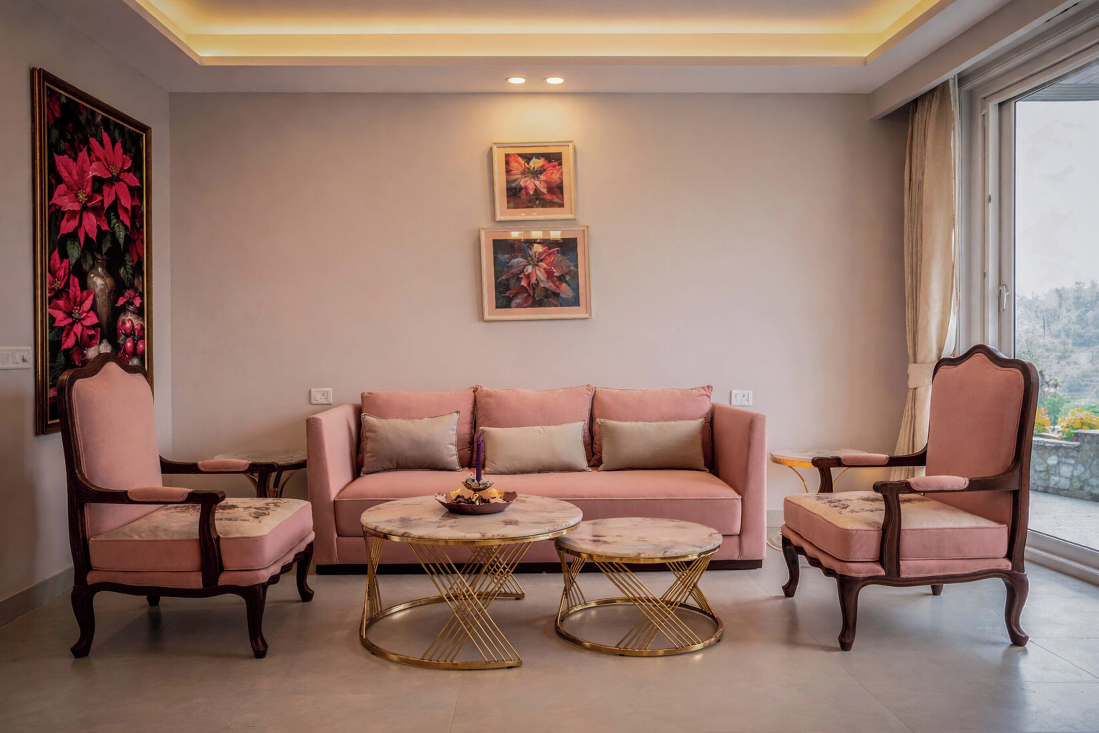 Una sala de estar con un sofá rosa, dos sillones y dos mesas redondas con marcos dorados.