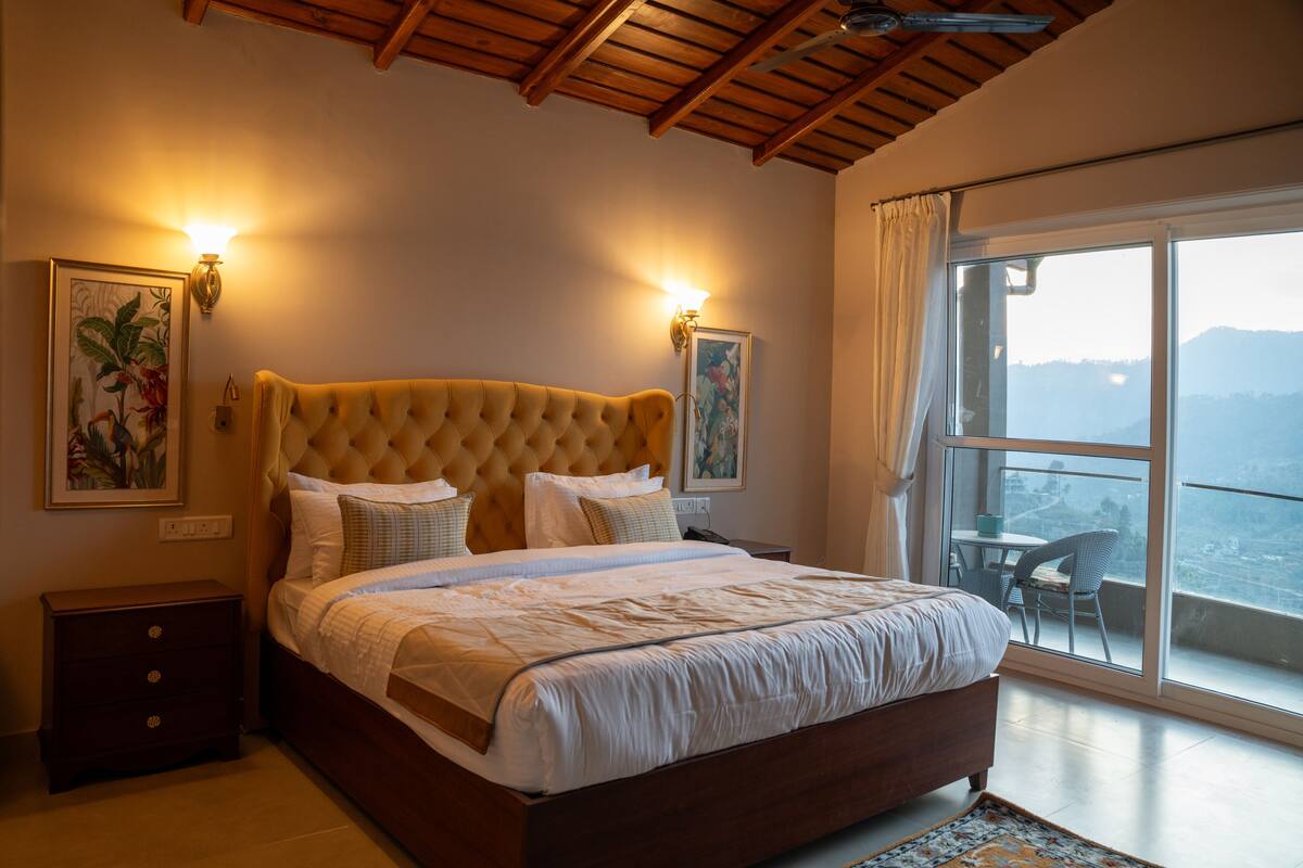 A bedroom with a large bed, two wall-mounted lights, a nightstand, a window with a view, and a ceiling fan.