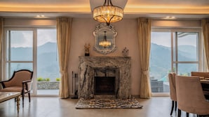 A room with a fireplace, a chandelier, and a view of mountains. - amã Stays & Trails Aryananda Villas, Dhari (Dhari)
