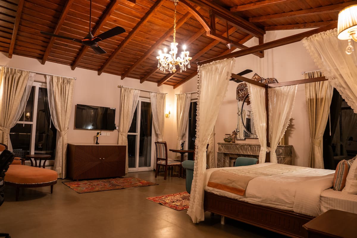 A bedroom with a wooden ceiling, a bed with a canopy, a television, and a desk with a chair.