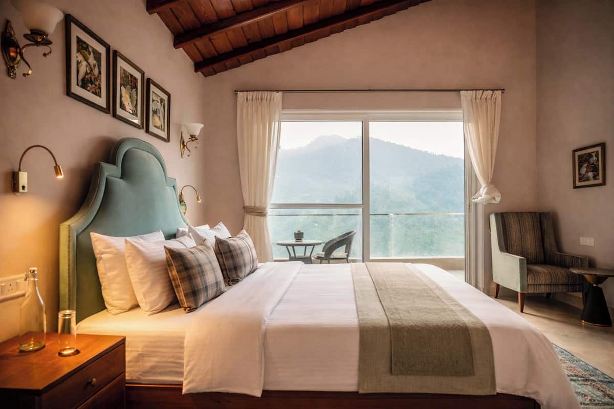 A bedroom with a large bed, a view of mountains, a chair, and a table.
