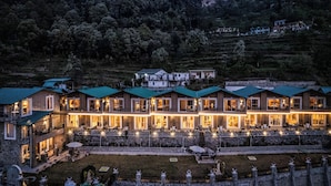 A multi-story hotel with a terrace and outdoor seating area, surrounded by a hilly landscape. - amã Stays & Trails Aryananda Villas, Dhari (Dhari)