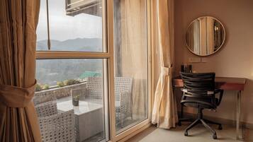 A room with a large window, a desk, a chair, and a round mirror on the wall.